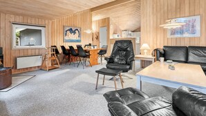 L’intérieur chaleureux d’un chalet comprend un coin repas, un canapé en cuir noir et une table à manger en bois.