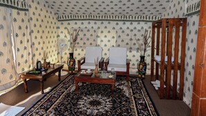 A room with patterned wallpaper, a wooden coffee table, two white armchairs, a patterned rug, and decorative vases. - Bookmark Shivir (Phulpur)