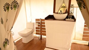 A bathroom with a white toilet, a wooden bench, a sink with a mirror, and a window with a view of a building. - Bookmark Shivir (Phulpur)