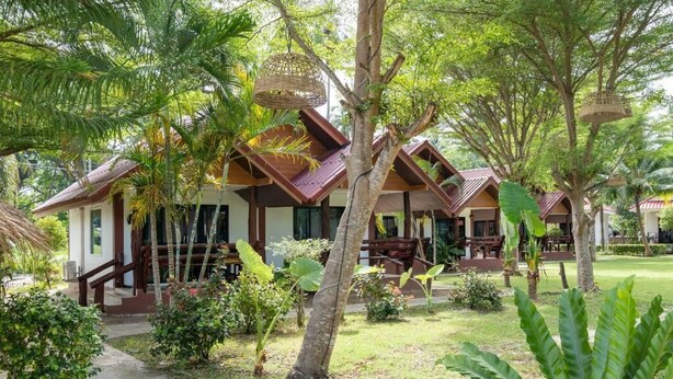 Un hôtel de style bungalow, doté d’un toit de chaume, entouré d’une végétation luxuriante et de palmiers.