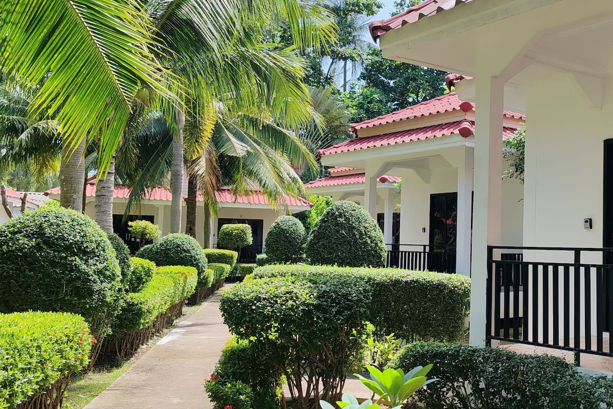 A series of white buildings with red roofs, surrounded by well-maintained hedges and palm trees.
