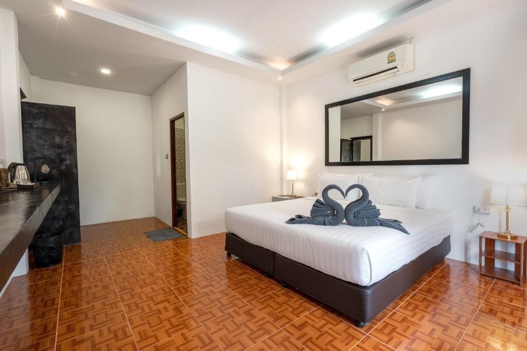 Hotelkamer met een bed, een spiegel, nachtkastje, lamp en een wandairconditioner.