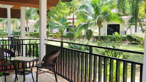 Un espace extérieur abrité, doté d’une table et de deux chaises, entouré d’une rambarde et offrant une vue sur un jardin bien entretenu, avec diverses plantes, et sur un bâtiment situé au loin.