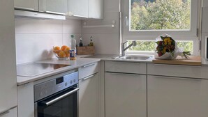 A modern kitchen with white cabinets, a built-in oven, a sink, and a window with a view of trees. - Vacation home Hirschle -Sauna, dogs, 3 bedrooms, 8 persons (Alpirsbach)