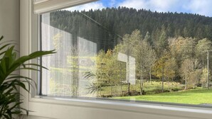 A window with a view of a forested hillside and a building in the background. - Vacation home Hirschle -Sauna, dogs, 3 bedrooms, 8 persons (Alpirsbach)