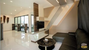 A modern living room with a flat-screen TV, a marble coffee table, a sofa, and a staircase. - Boathouse Boutique Riverside (Nakhon Chai Si)