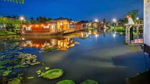 A waterfront property with floating homes, a calm lake, and a person standing on a balcony. - Boathouse Boutique Riverside (Nakhon Chai Si)