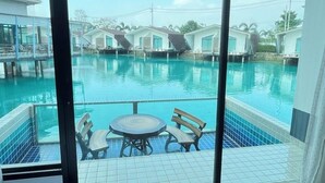 A hotel room with a large window overlooking a swimming pool and a view of the resort's buildings. - Boathouse Boutique Riverside (Nakhon Chai Si)