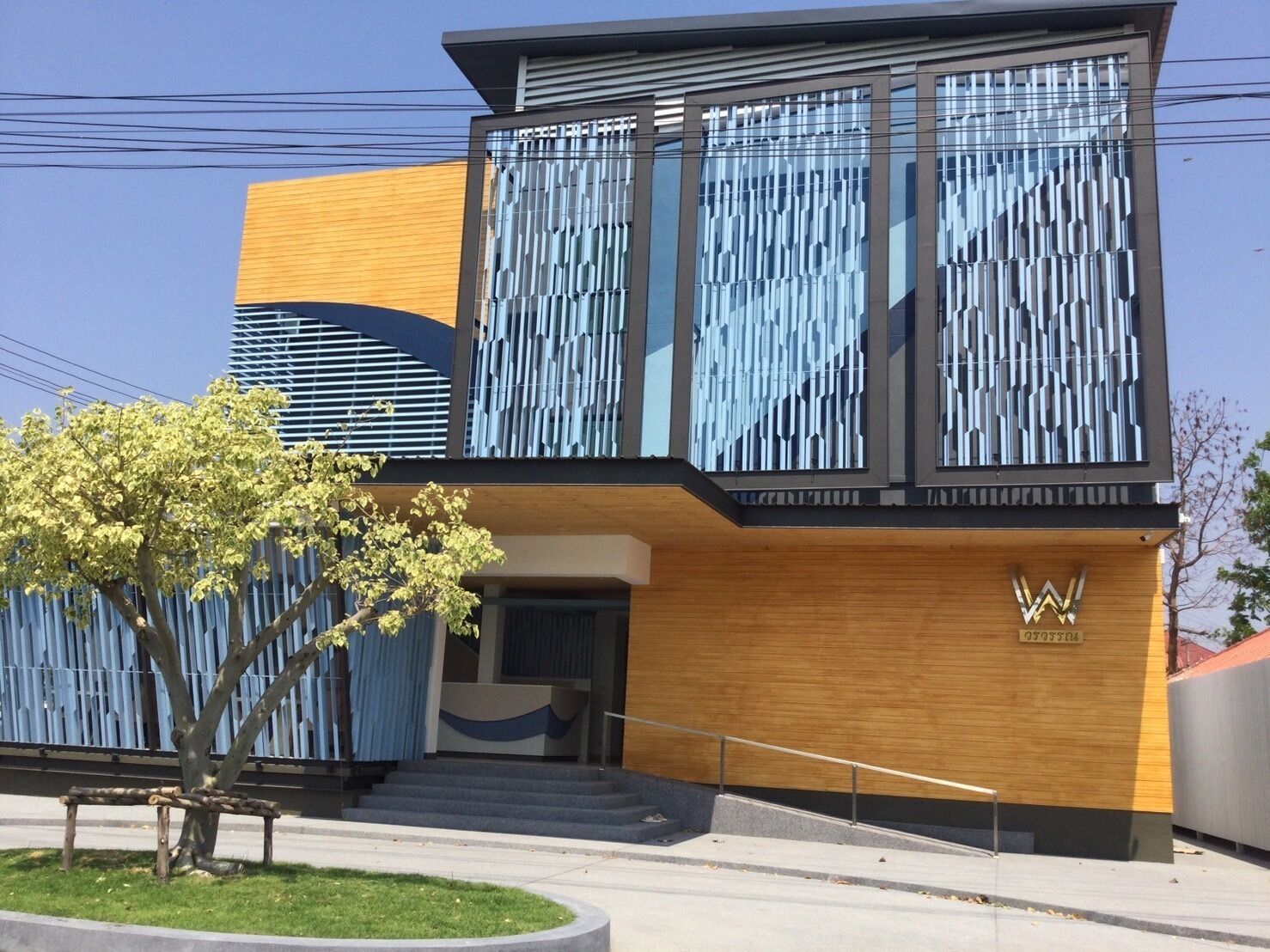 A modern building with a wooden facade, a large entrance with steps, and a logo on the side.