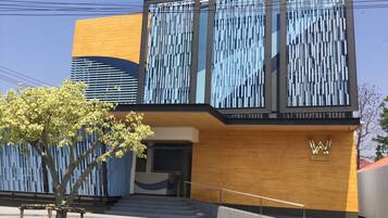 A modern building with a wooden facade, a large entrance with steps, and a logo on the side.