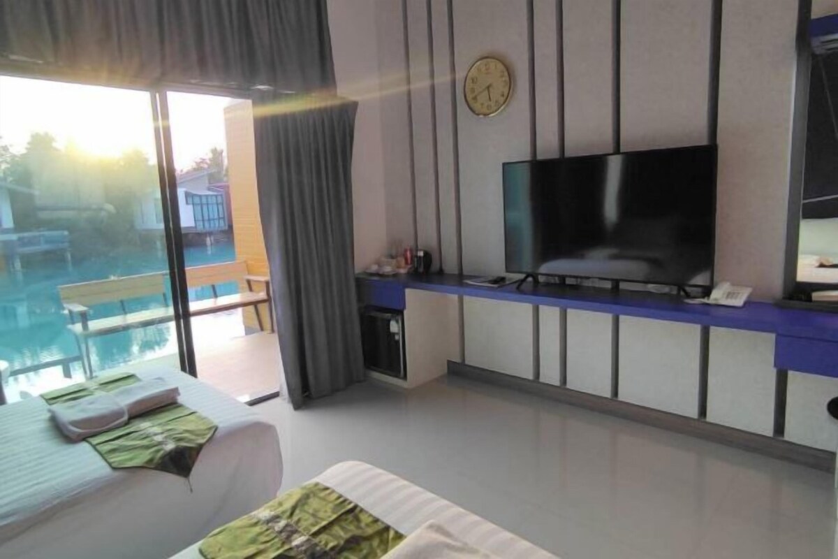 Ein modernes Hotelzimmer mit großem Fernseher, Schreibtisch mit Telefon und Blick auf einen Außenpool.