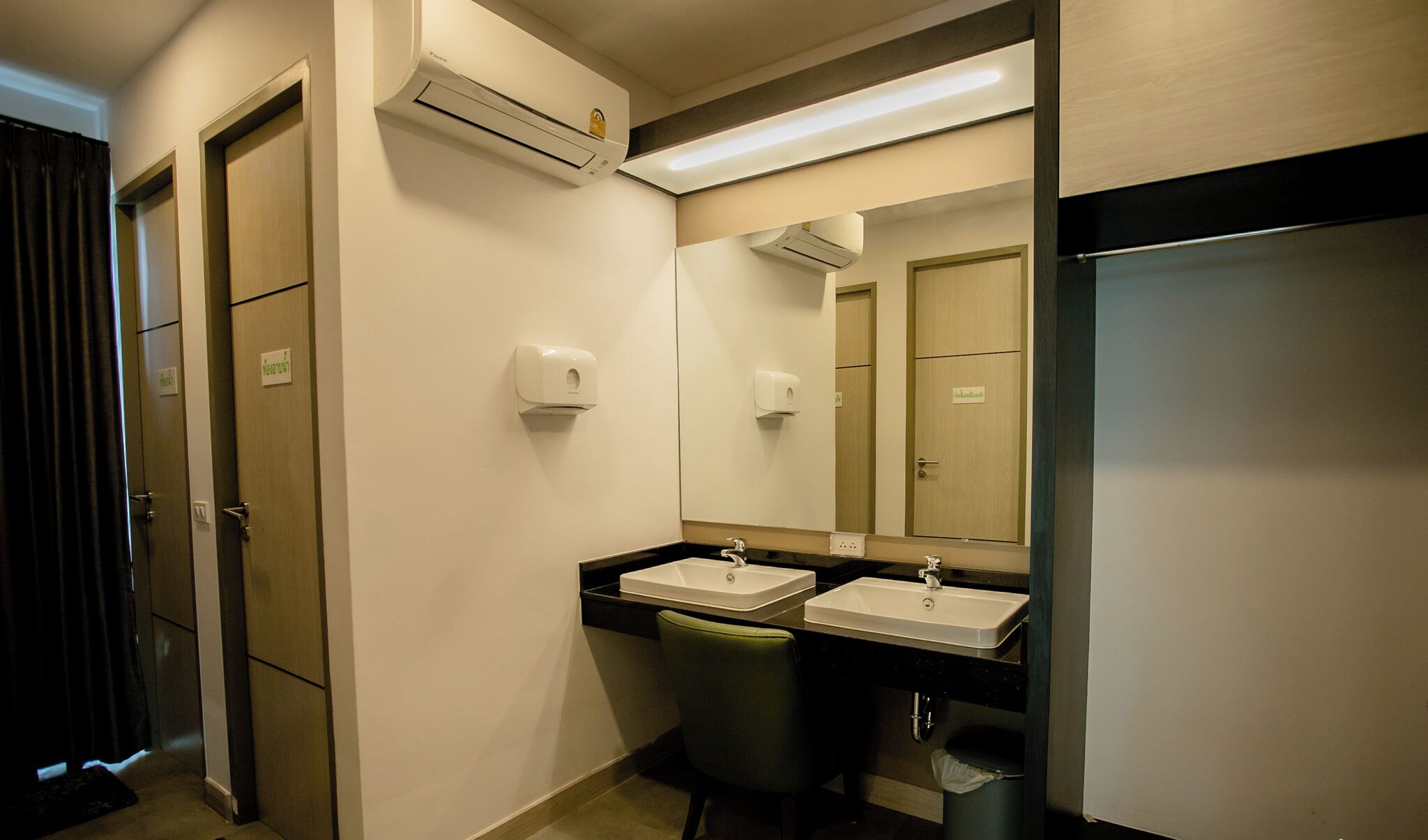 Een hotelbadkamer met twee wasbakken, een spiegel, een airconditioning en een prullenbak.