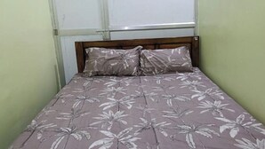 A single bed with a floral-patterned bedspread and matching pillows, a wooden headboard, and a window with blinds. - Goroomgo Anand Atithi Bhawan Puri (Puri)