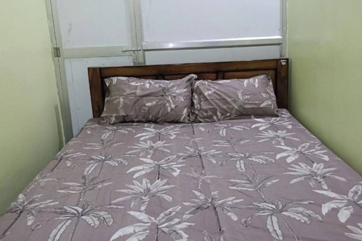 Una cama individual con una colcha de estampado floral y almohadas a juego, un cabecero de madera y una ventana con persianas.