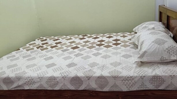 A single bed with a patterned bedspread and pillows, a wooden headboard, and a plain wall. - Goroomgo Anand Atithi Bhawan Puri (Puri)