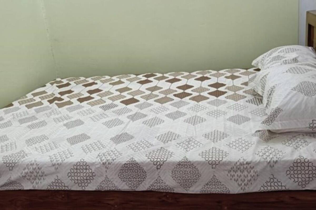 Una cama individual con una colcha y almohadas estampadas, un cabecero de madera y una pared lisa.