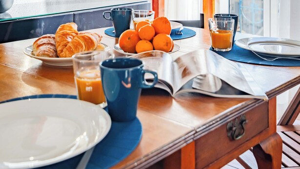 A breakfast table with croissants, oranges, and juice, set in a room with a large window and wooden beams. - Bica's River View Duplex (Lisbon)