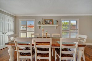 A dining room with a wooden table and white chairs, a decorative sign on the wall, and a window with blinds. - The Crown House 4b Pool Home 6 Mins to IR Beach (Largo)