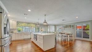 Una cocina amplia con armarios blancos, una isla central y un comedor con sillas blancas.