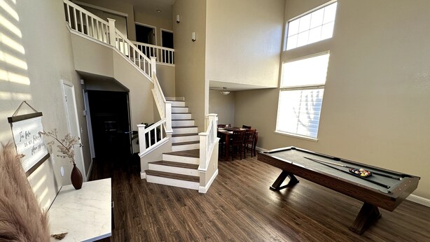 Un vaste espace de vie comprenant une table de billard, une table à manger avec des chaises et un escalier menant à un niveau supérieur.