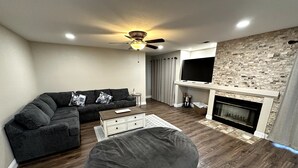 Un salon comprenant un canapé d’angle, un fauteuil en forme de poire, une cheminée et un ventilateur de plafond.