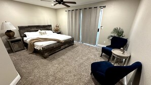 Une chambre à coucher comprenant un lit, une table de chevet, une chaise, une lampe, un ventilateur de plafond et une vue sur l’extérieur.