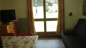 Una habitación con cama, televisión, sofá y ventana con cortinas.