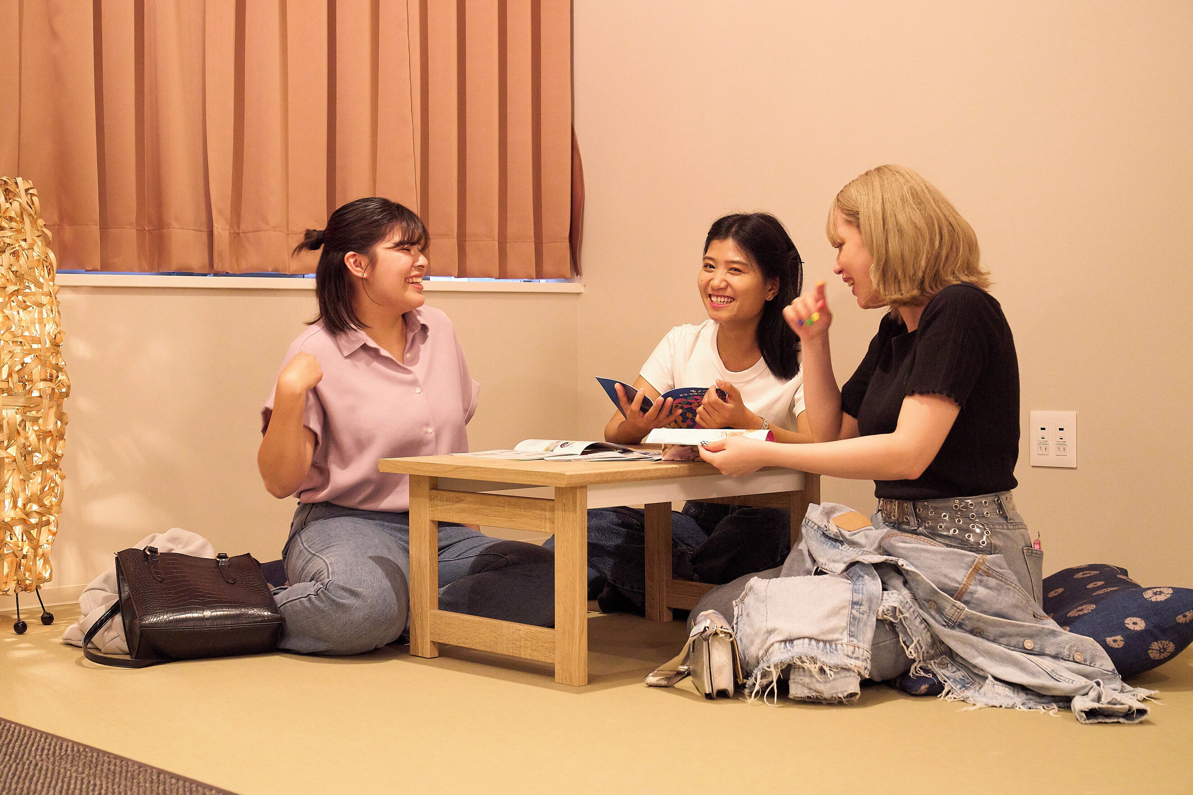 Three people sitting on the floor in a room with a table, a window with blinds, and a power outlet on the wall.