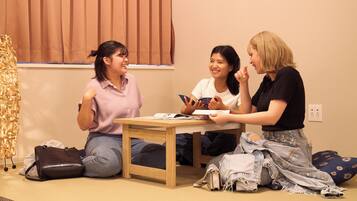 Three people sitting on the floor in a room with a table, a window with blinds, and a power outlet on the wall.