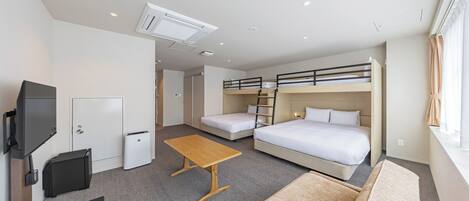 A hotel room with a bunk bed, a single bed, a desk, a chair, a TV, and a small table.