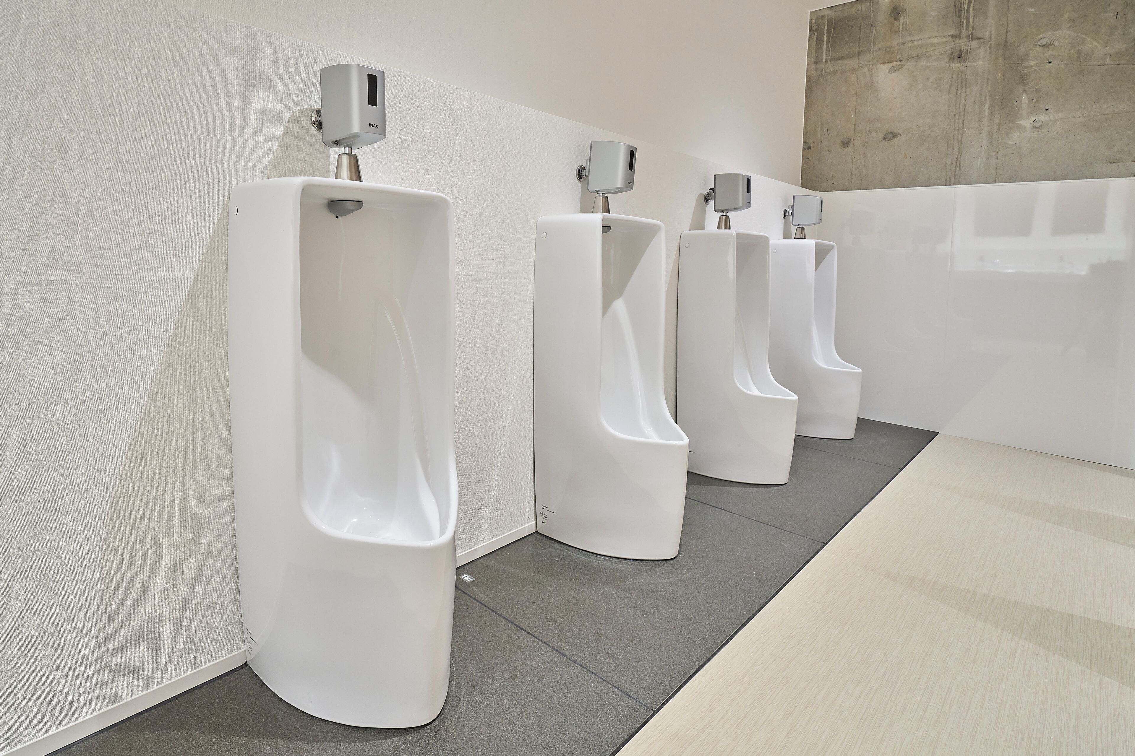 A row of white urinals in a restroom with a plain wall and a concrete accent.