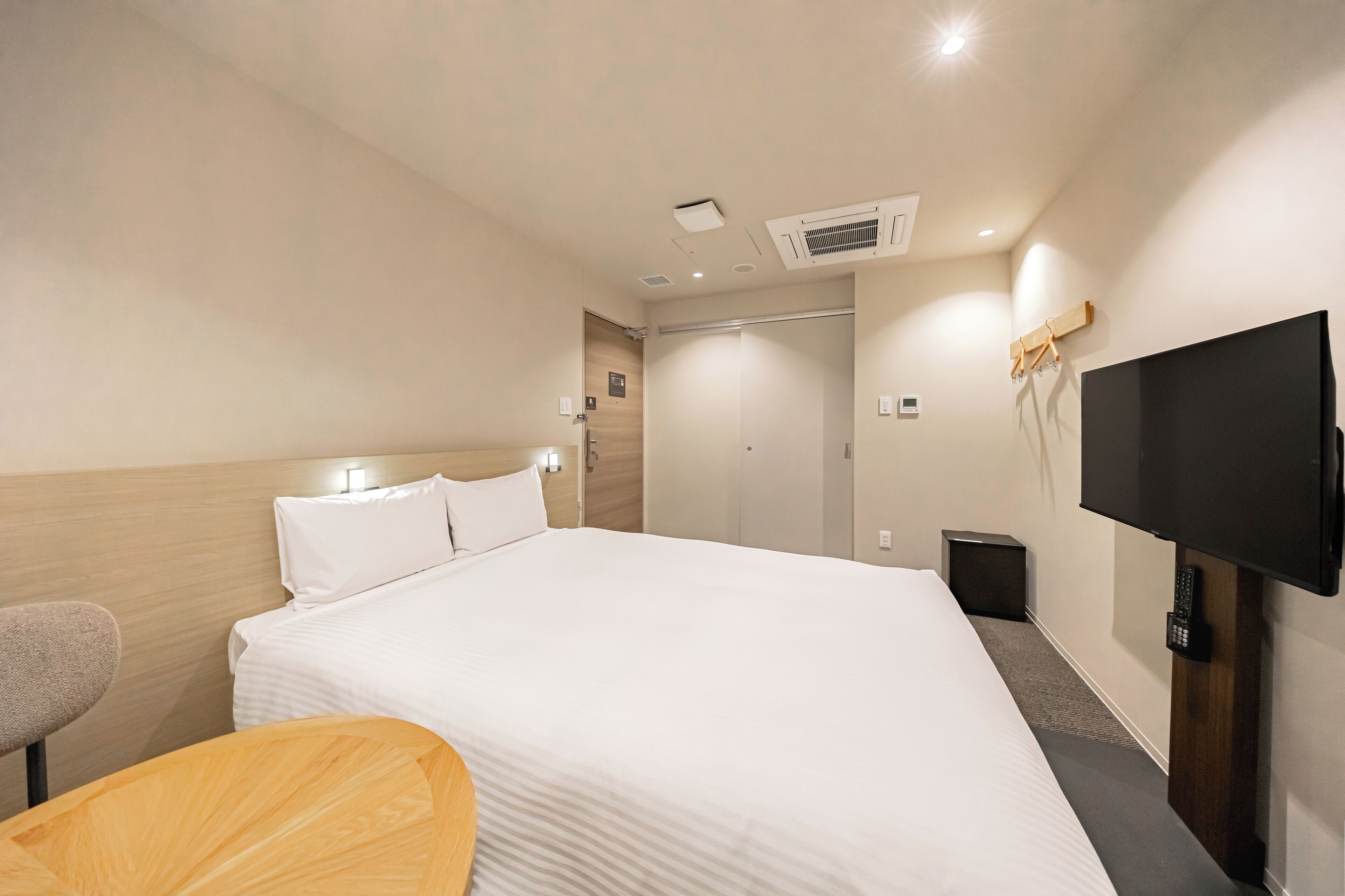 A hotel room with a large bed, a TV mounted on the wall, and a wooden chair.