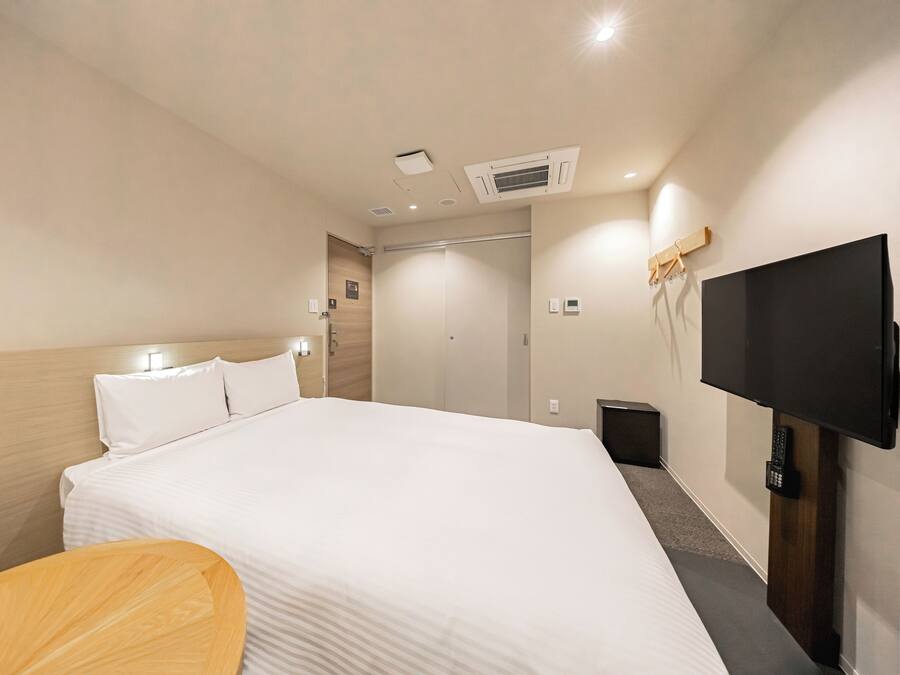 A hotel room with a large bed, a TV mounted on the wall, and a wooden chair.