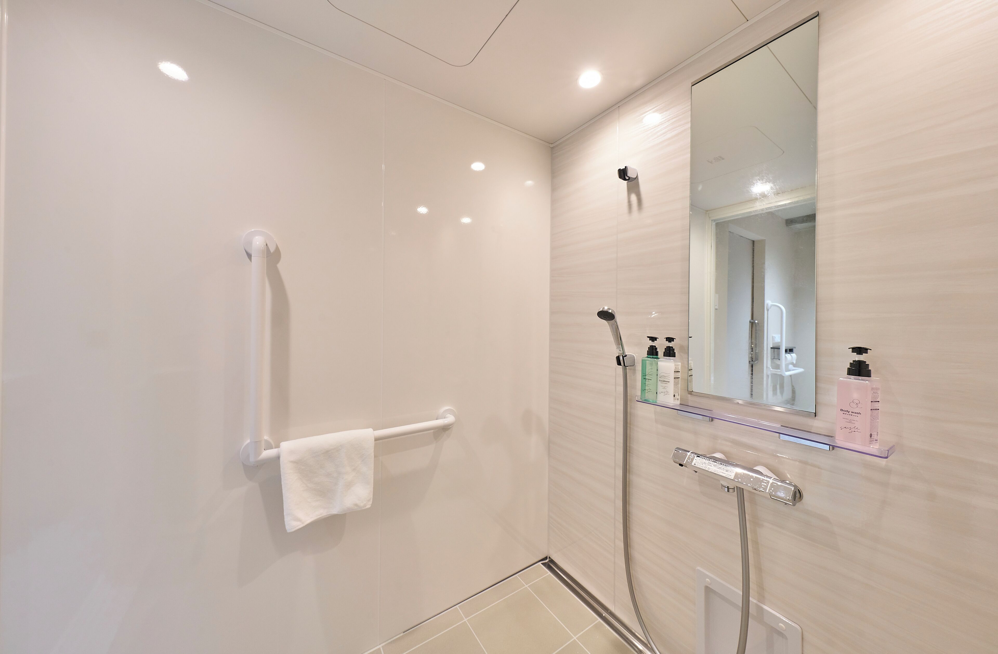A modern bathroom with a glass shower enclosure, a white towel rack, and a mirror with a shelf holding toiletries.