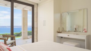 A bedroom with a large bed, a vanity with a mirror, and a view of the sea. - Miraida Exclusive Residence (Apokoronos)