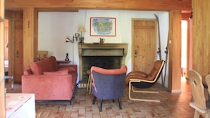 A cozy living room with a fireplace, a sofa, a chair, and a wooden ceiling.