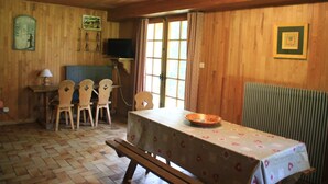A wooden-paneled room with a dining table, chairs, a bench, a television, and a radiator.