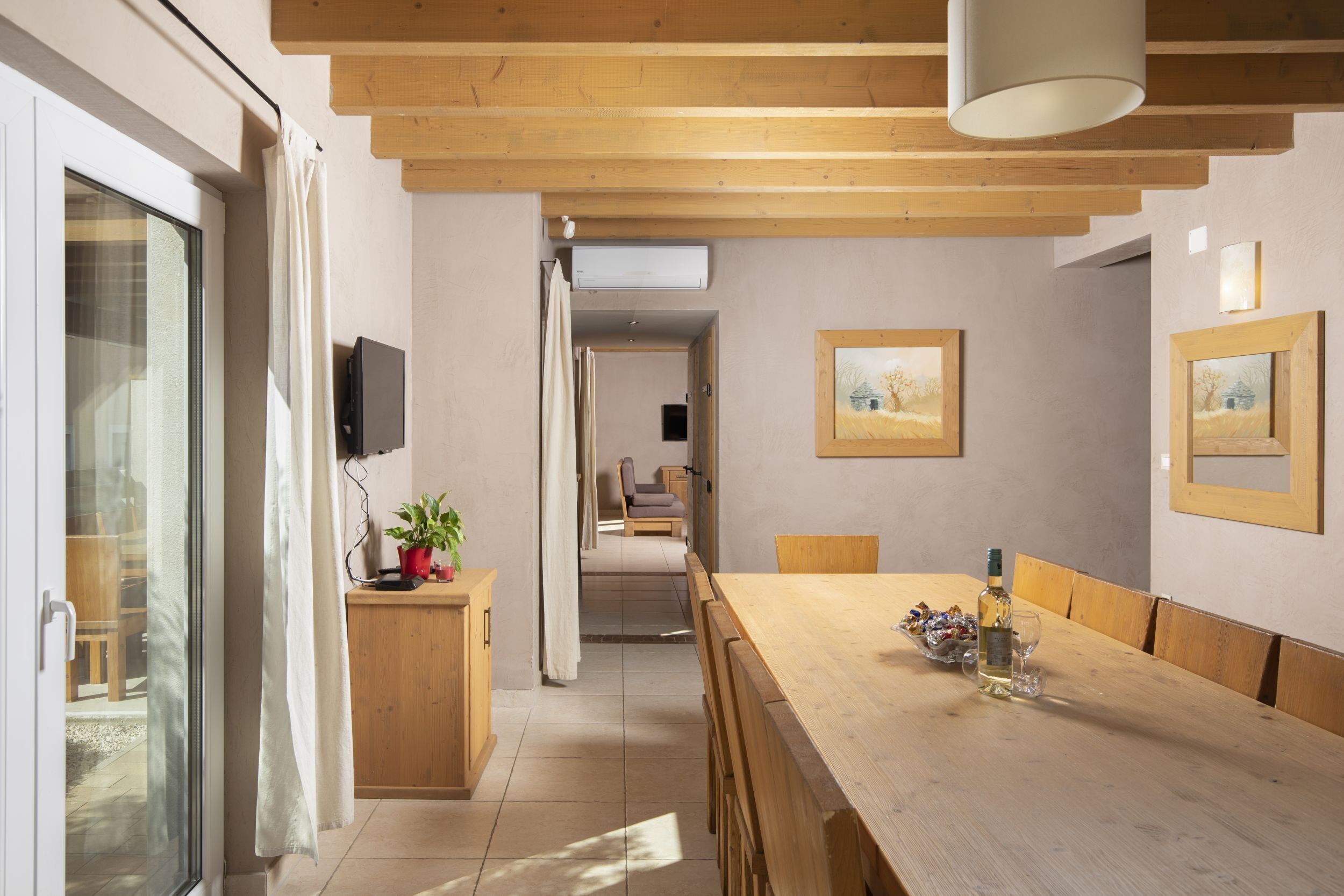 Un coin repas avec une table en bois, des chaises et une plante en pot. Un téléviseur est fixé au mur et des tableaux encadrés sont accrochés au-dessus de la table.