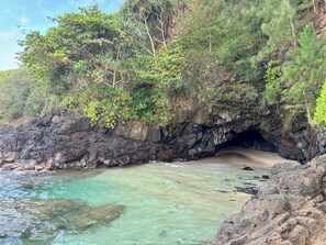 L’entrée d’une grotte côtière, avec une eau turquoise et limpide, entourée d’une végétation luxuriante et d’un paysage rocheux.