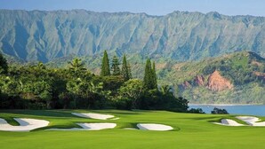 Un campo de golf con búnkeres de arena y montañas y un lago al fondo.