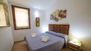 Un dormitorio con cama, una mesita de noche con lámpara, una ventana con persianas y una pared decorada con un panel y una obra de arte.