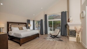 A spacious bedroom with a large bed, a chair, a fireplace, and a view of the outdoors.