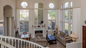 A spacious living room with a fireplace, a staircase, and large windows offering views of the outdoors.