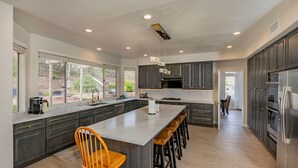 A modern kitchen with dark cabinets, a large island with stools, and a view through the windows.