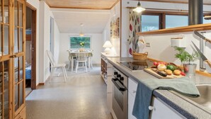 Een moderne keuken met houten balken, een eethoek met een tafel en stoelen, en uitzicht op groen.
