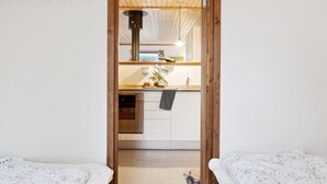 Een slaapkamer met twee bedden, een houten plafond en uitzicht op een keuken met een spoelbak en kasten.