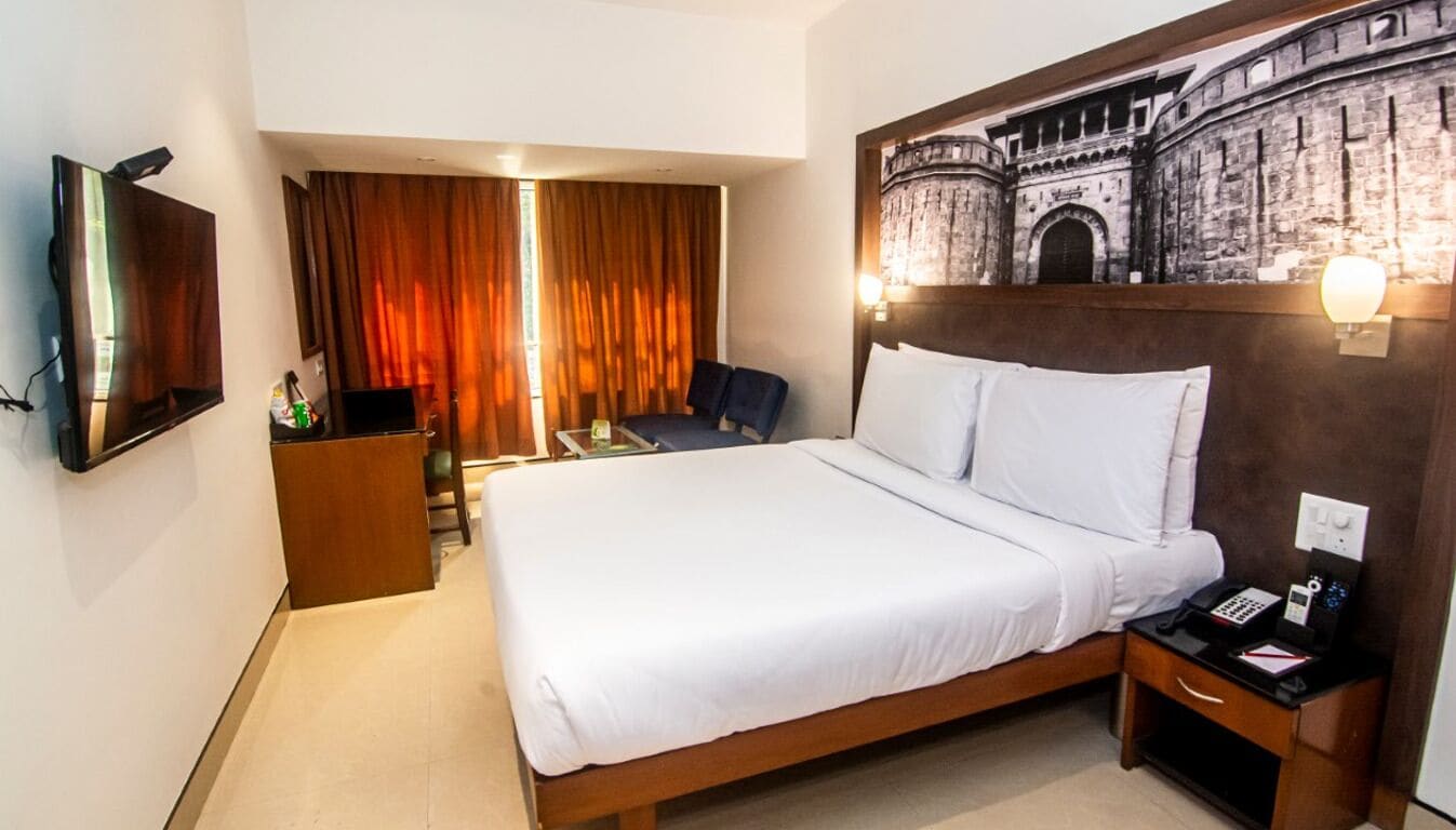 Ein Hotelzimmer mit einem Bett, einem Schreibtisch, einem Sessel, einem Fernseher und einem Wandbild.