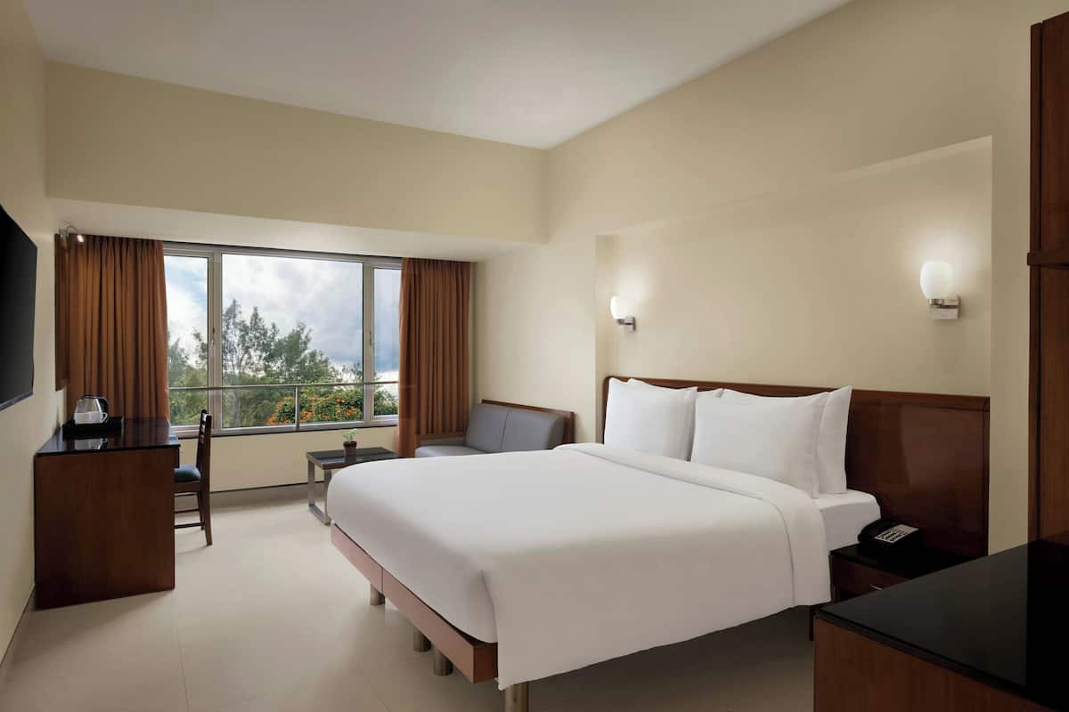 Ein Hotelzimmer mit einem großen Bett, einem Schreibtisch, einem Stuhl, einem Fernseher und einem Balkon mit Vorhängen.