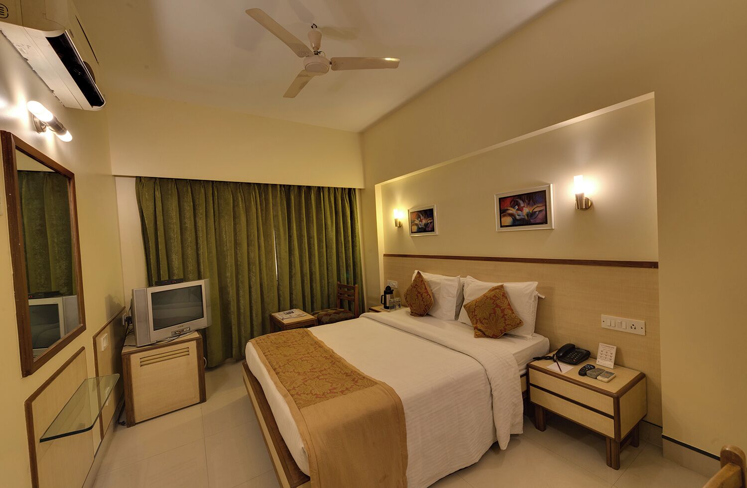 A hotel room with a bed, a television, a desk, a chair, a nightstand, a phone, and a ceiling fan.
