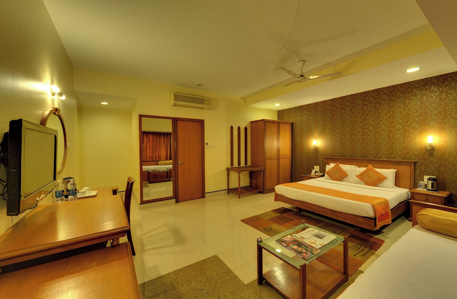 A hotel room with a bed, a desk, a chair, a television, and a mirror.